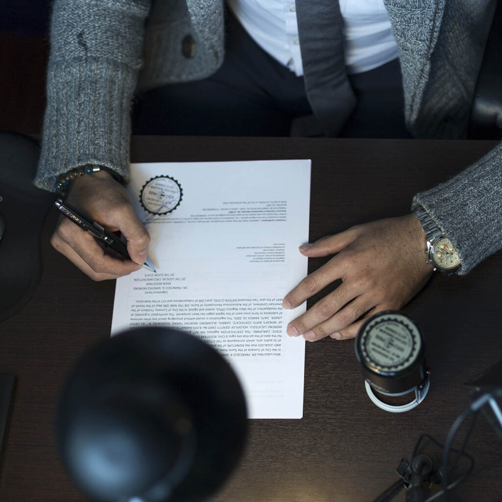 Manos de ejecutivo firmando documentos en escritorio corporativo durante proceso administrativo